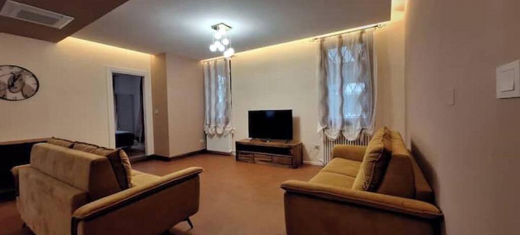 Een woonkamer met twee banken, een televisietoestel op een dressoir en een deur naar een andere kamer.