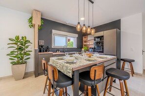 Ett modernt kök med en central köksö, barstolar och ett matbord med plats för fyra personer.