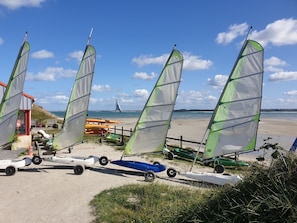 A beach with multiple windsurfing boards and sails, a wooden fence, and a distant view of the sea. - "Ti Zen" Townhouse, All the Comforts, Air Conditioning, Beach 10 Minutes Away (Lesneven)