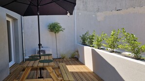 Eine Holzterrasse mit einem schwarzen Sonnenschirm, einem kleinen Tisch und Kübelpflanzen.