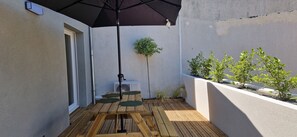 En träveranda med ett svart parasoll, ett litet bord och krukväxter.