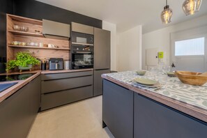 A modern kitchen with built-in appliances, wooden shelves, and a central island with a bowl and plates. - "Ti Zen" Townhouse, All the Comforts, Air Conditioning, Beach 10 Minutes Away (Lesneven)