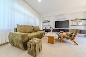 Ett modernt vardagsrum med en soffgrupp, ett soffbord och en fåtölj. En platt-TV är monterad på väggen och det finns ett litet bord med dekorativa föremål.