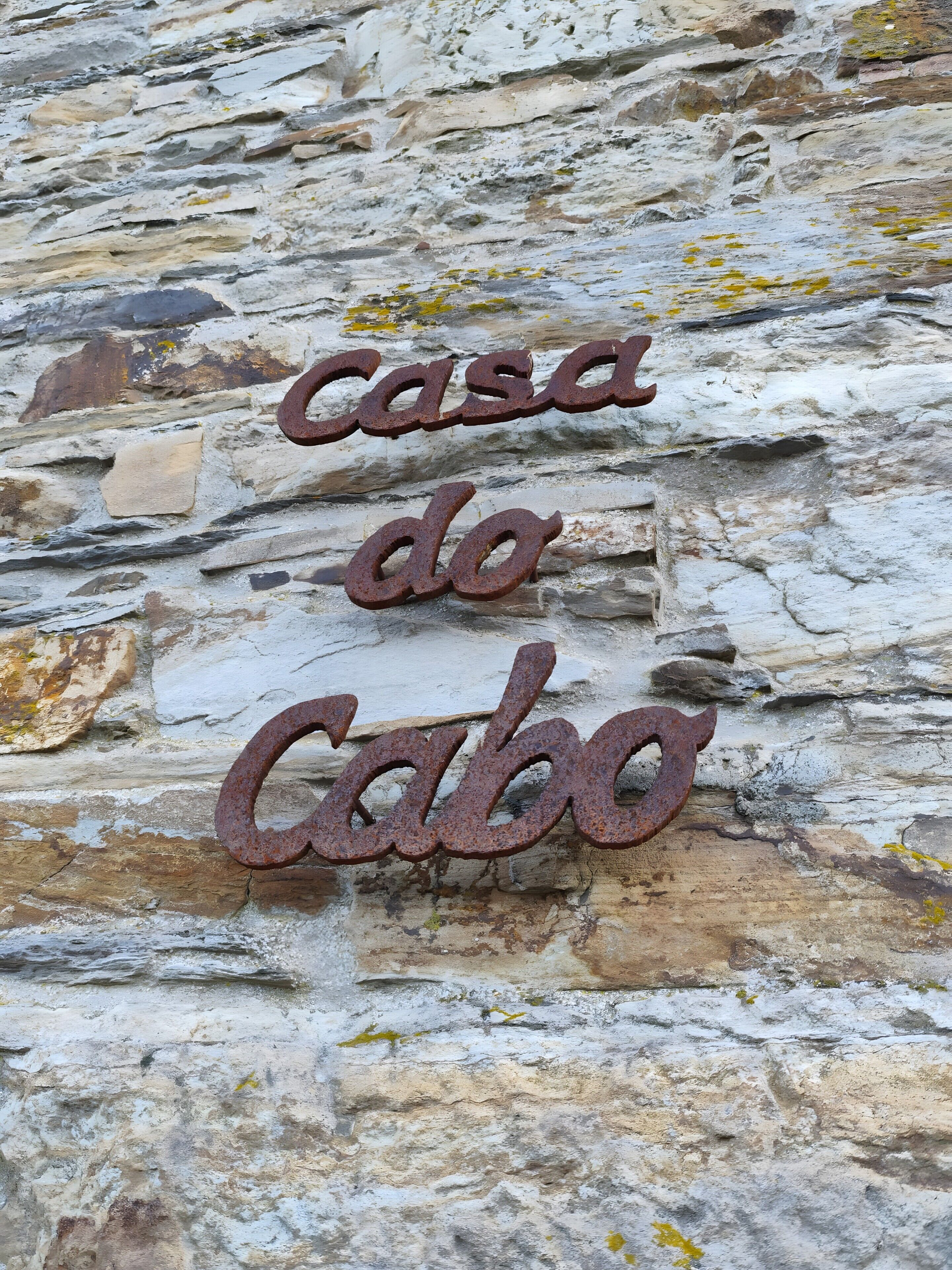 Een rustieke stenen muur met een metalen bord waarop 'casa do Cabo' staat.
