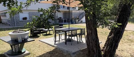 An outdoor patio area with a table and chairs, surrounded by trees and a building in the background.