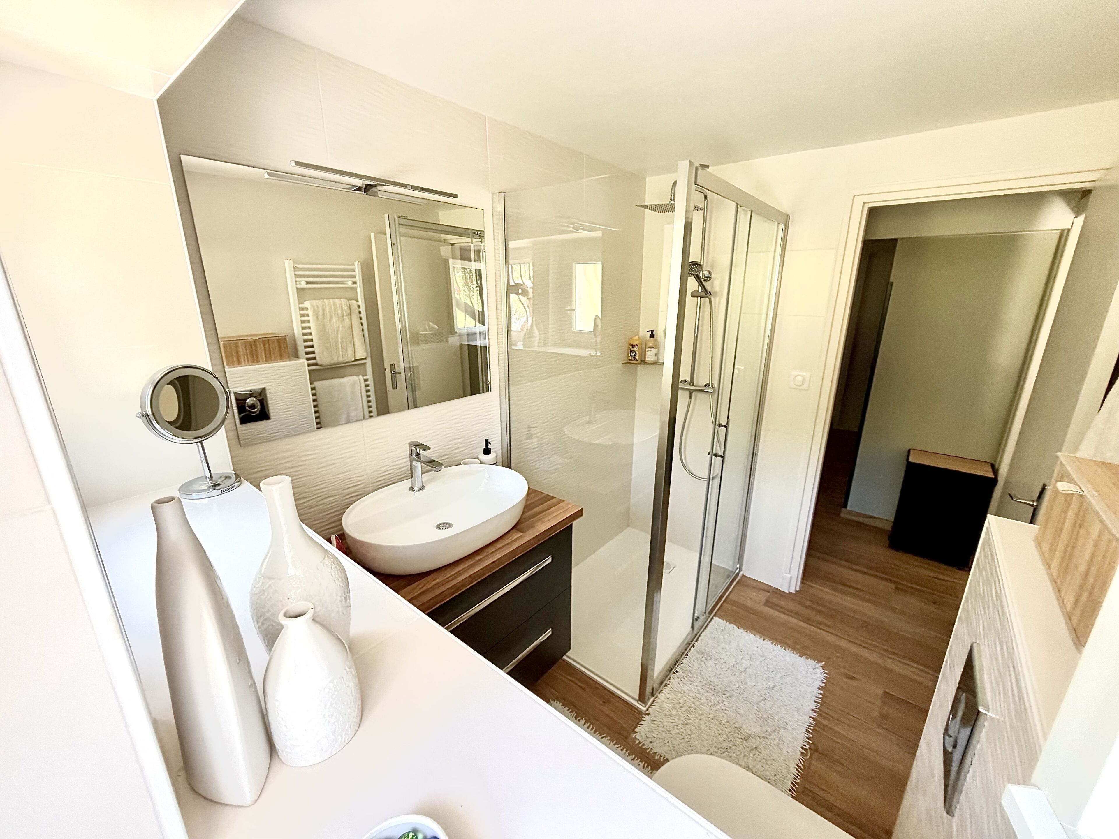 A modern bathroom with a glass-enclosed shower, a large mirror, and a white sink.
