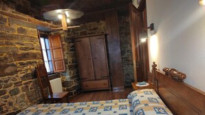 Un dormitorio con pared de piedra, muebles de madera y colcha estampada.