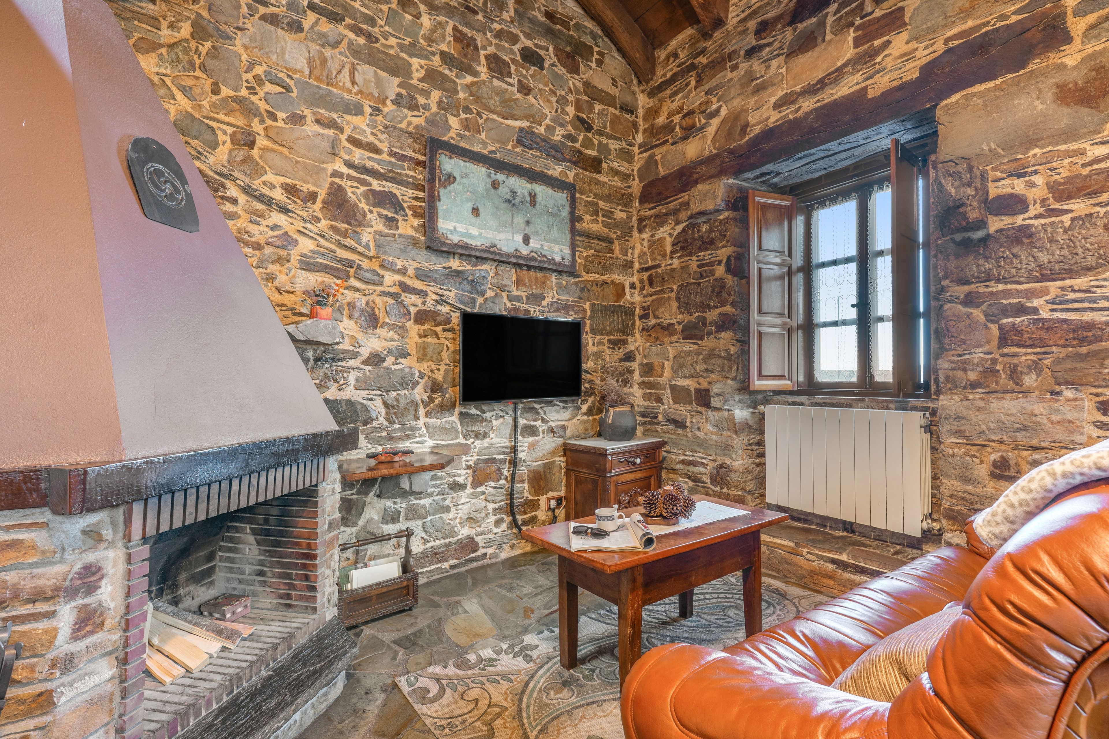 Una habitación con paredes de piedra, una chimenea, un televisor, una ventana y un sofá de cuero.