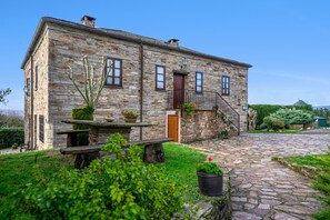 A stone building with a wooden bench, potted plants, and a stone pathway.