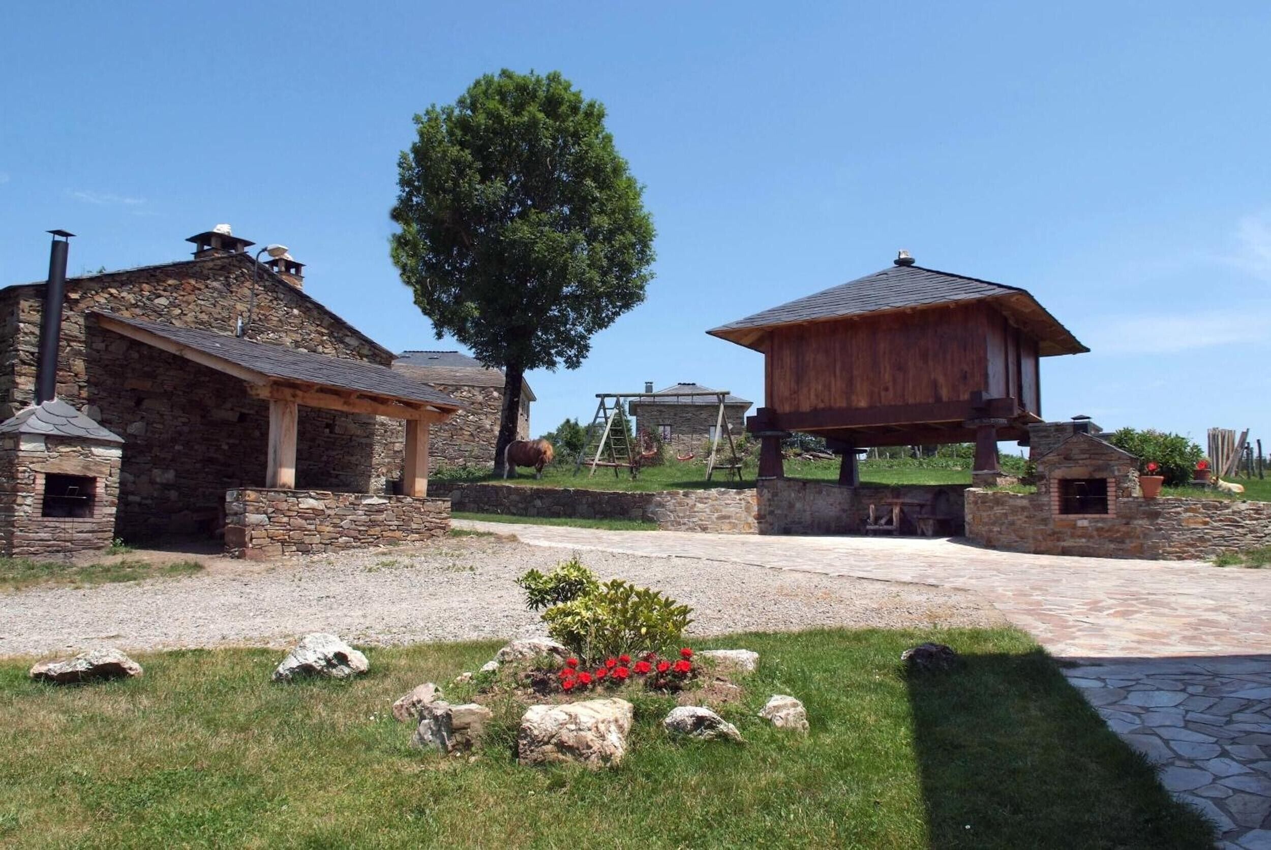 A stone building with a chimney, a wooden structure with a sloped roof, and a large tree in the center.