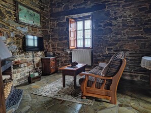A stone-walled room with a wooden sofa, a television, and a window with curtains. - Apartment 'Puleiro' with Mountain View, Shared Terrace and Wi-Fi (Braña)