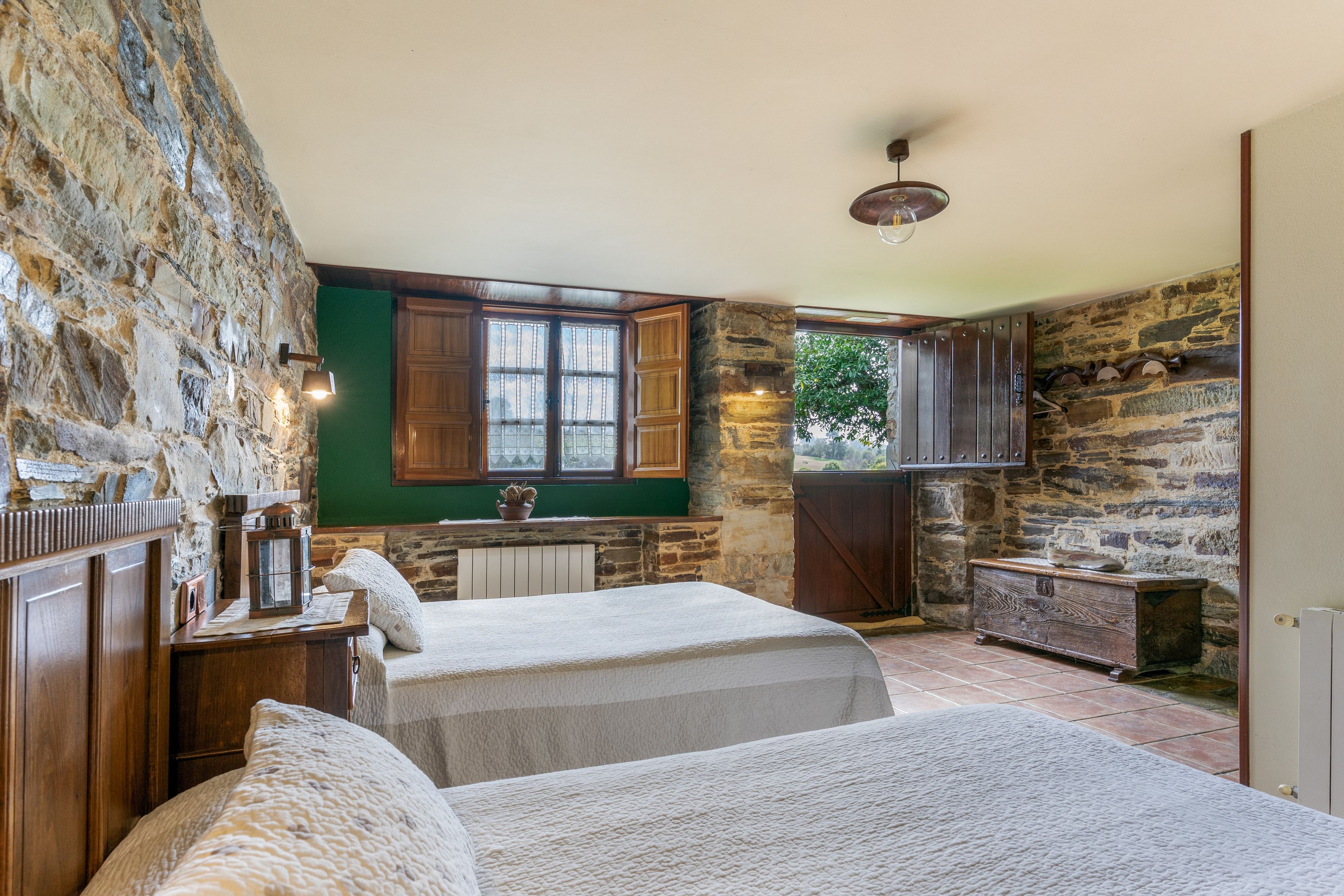Un dormitorio rústico con paredes de piedra, muebles de madera y vistas al verdor exterior.