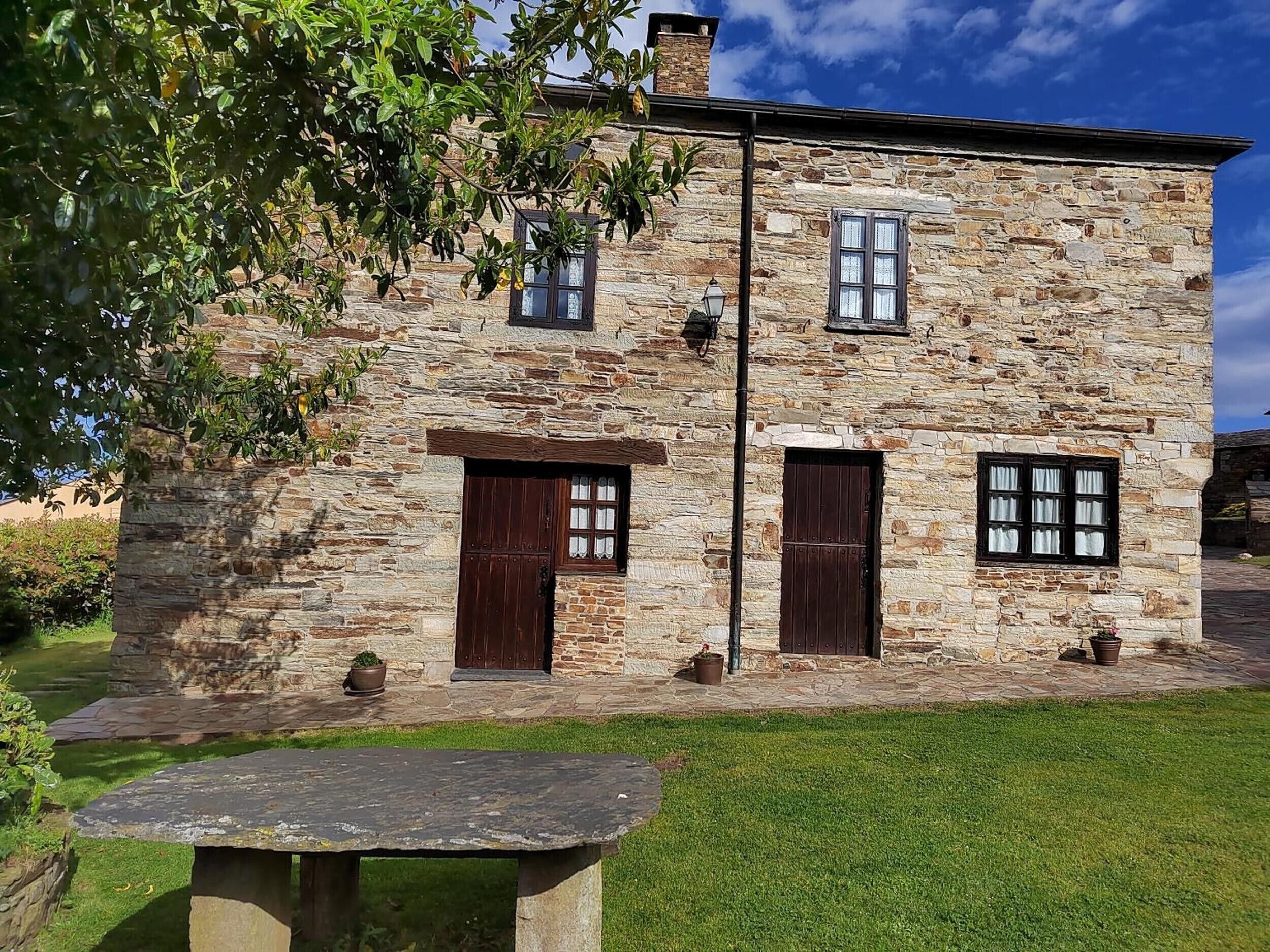 A stone building with two windows and a door, a stone bench in the foreground, and a clear sky.