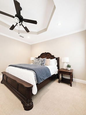 Une chambre à coucher avec un grand lit, un ventilateur de plafond, deux tables de chevet avec des lampes et un sol recouvert de moquette.
