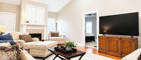 Un salón amplio con ventilador de techo, chimenea, televisor y un ventanal grande.