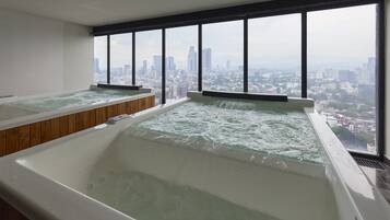 A room with two hot tubs and a city view.