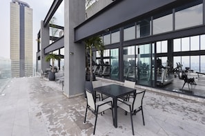 Terraço no telhado com área de estar externa, equipamentos de ginástica e vista para a paisagem urbana.