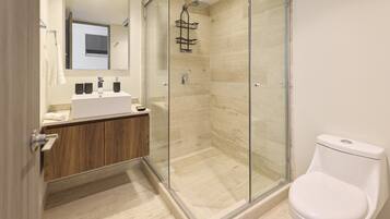 Un baño moderno con ducha envuelta en vidrio, inodoro blanco y tocador de madera con espejo.