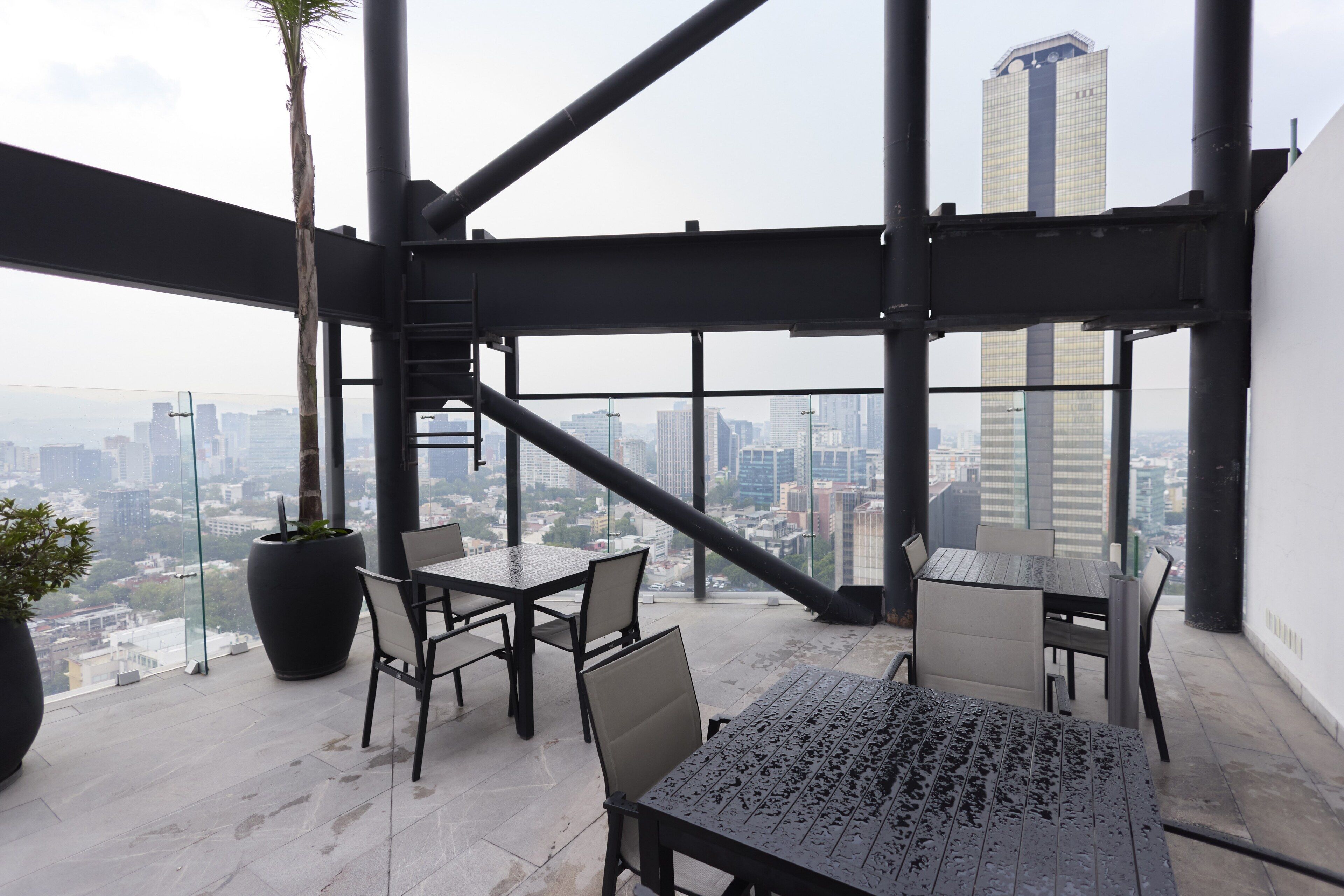 A high-rise building with a terrace featuring a table and chairs, a potted plant, and a view of the cityscape.