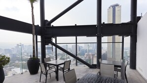 Un edificio de gran altura con una terraza que tiene una mesa, sillas, una planta en maceta y vistas de la ciudad.