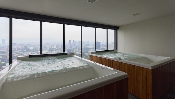 Dos tinas de hidromasaje en una habitación con ventanas amplias que dan a un paisaje urbano.