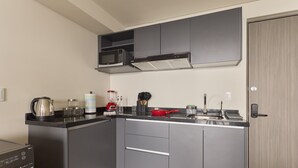 Cocina compacta con armarios grises, microondas, hervidor y una sartén roja sobre la encimera.