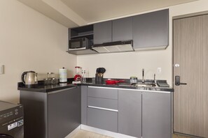 Cozinha compacta com armários cinza, micro-ondas, chaleira e uma frigideira vermelha sobre a bancada.