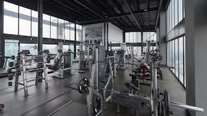 Un gimnasio con diverso equipo de ejercicio, ventanas amplias y un techo alto.