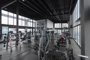 Academia com diversos equipamentos de exercício, janelas amplas e pé-direito alto.