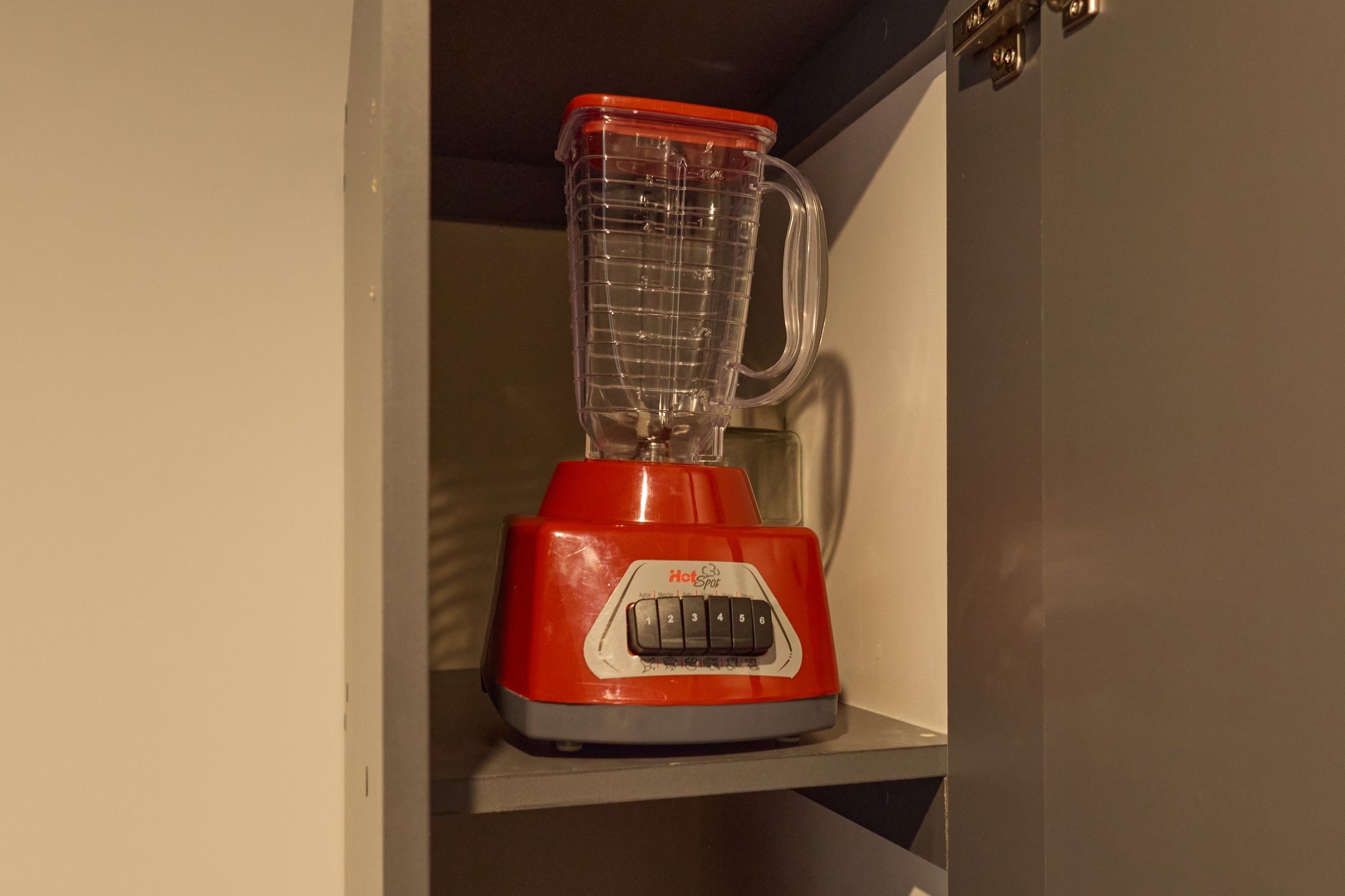 Een rode blender staat op een witte plank in een keuken.