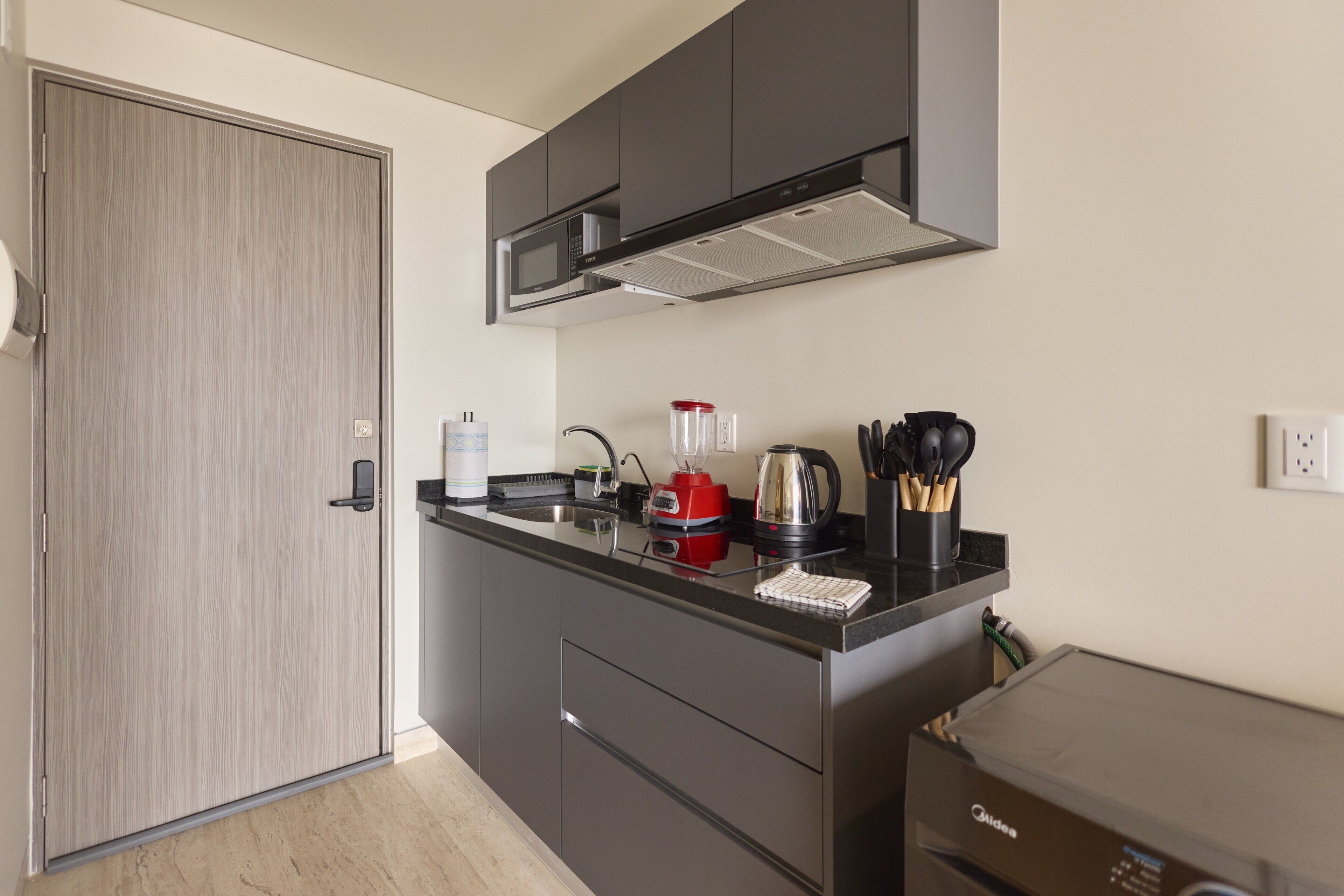 Una cucina compatta con forno a microonde, bollitore e macchina del caffè sul ripiano.