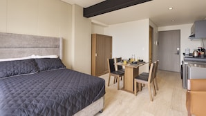 Un dormitorio moderno con una cama grande, un armario de madera y una zona de kitchenette con una mesa y sillas.