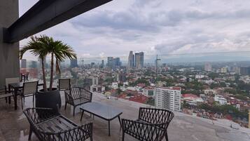 A terrace with outdoor furniture, a palm tree, and a cityscape view.