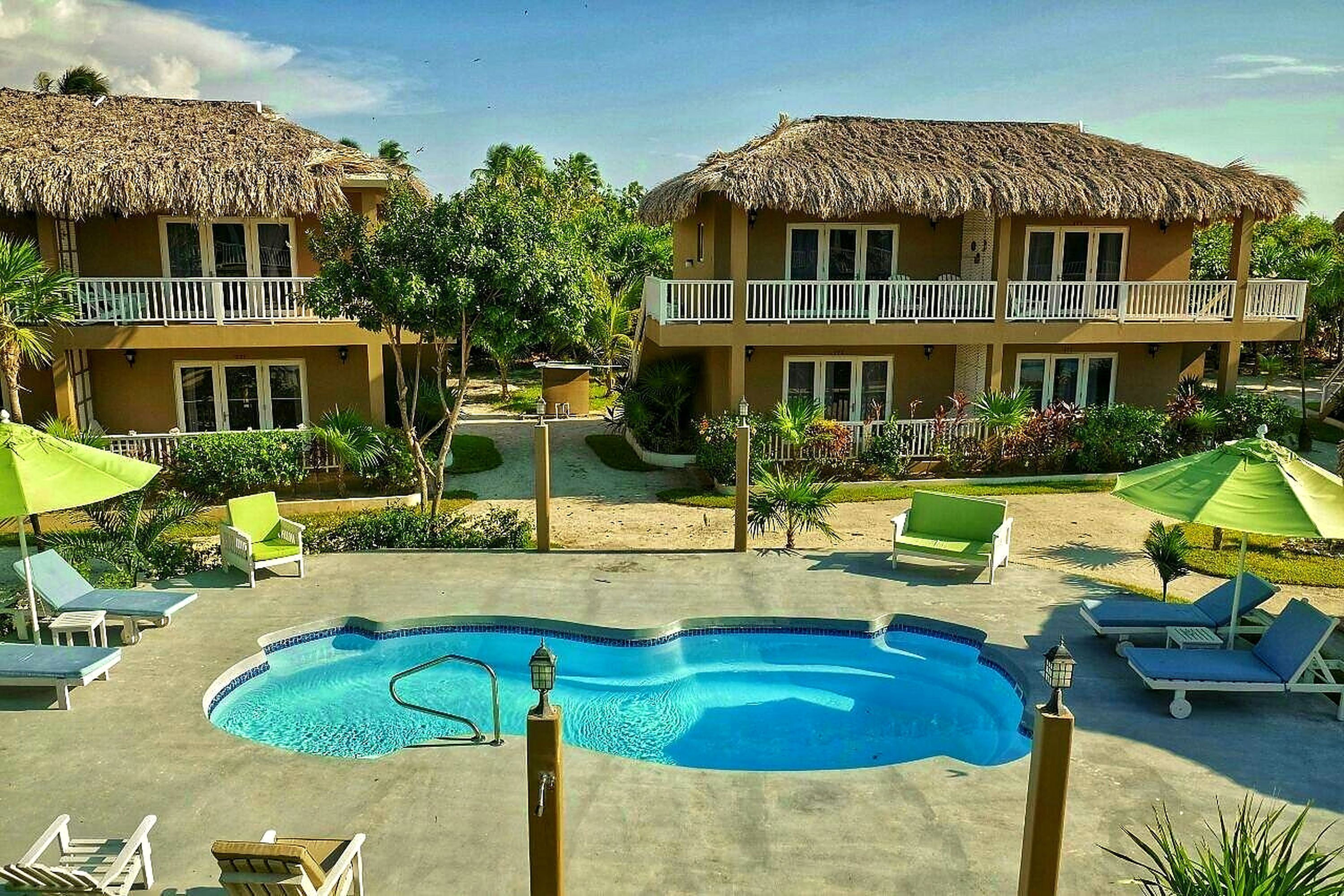A hotel with a pool, lounge chairs, and thatched-roof buildings.