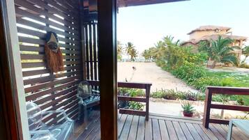 A wooden deck with a glass door leading to a patio area with a view of a beach and palm trees.