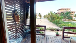 Una terraza de madera con una puerta de vidrio que da a un patio con vista a una playa y palmeras.