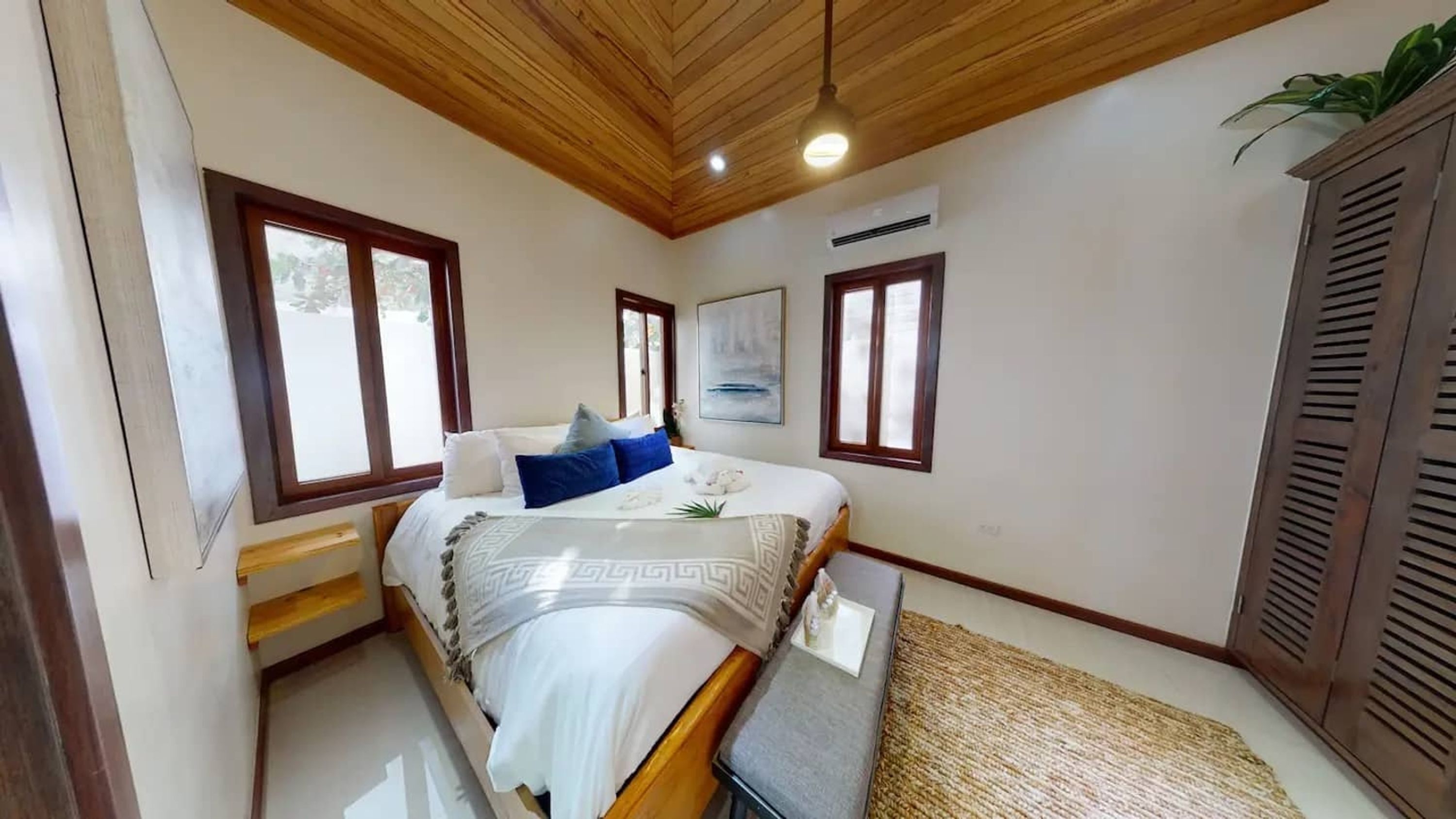 Un dormitorio con cama, mesita de noche, ventana y aire acondicionado de pared.