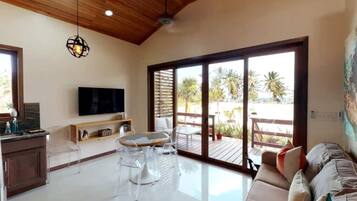 Un amplio salón con un gran ventanal corredera que da a una terraza exterior, un televisor de pantalla plana montado en la pared y un techo de madera.