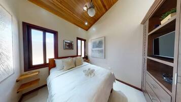 Un dormitorio con techo de madera, una cama con ropa blanca, una ventana, una mesita de noche y un televisor sobre una estantería.