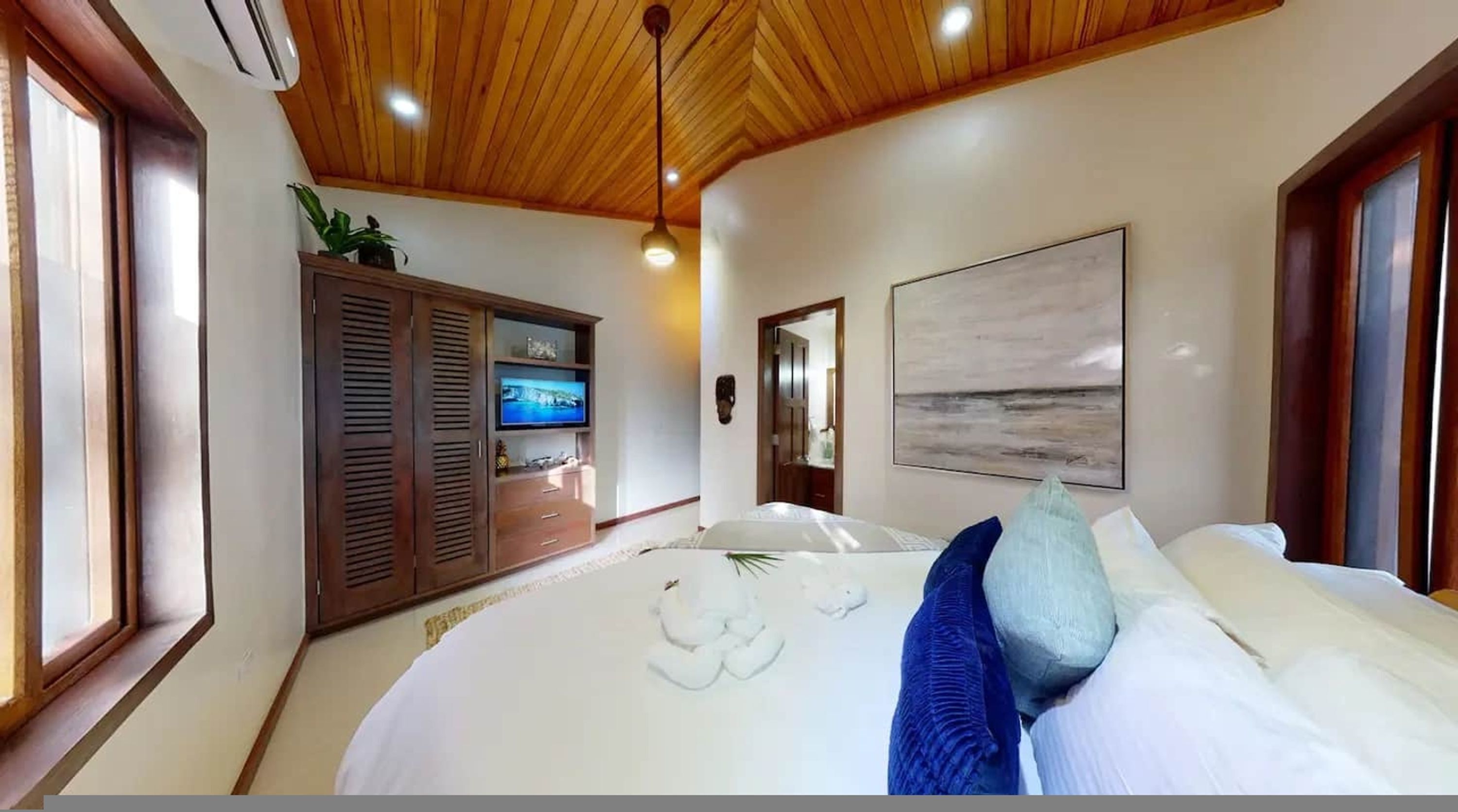 A bedroom with a bed, a TV, wooden ceiling, and a painting on the wall.