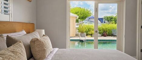 A bedroom with a large bed, a view of a swimming pool, and a door leading outside.