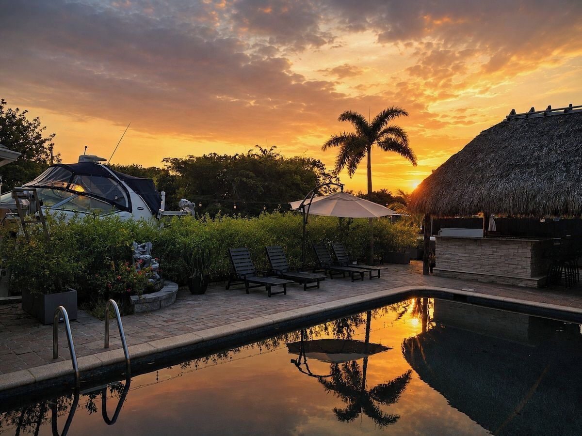 Ein Poolbereich mit Liegestühlen, einer strohgedeckten Struktur und einem Sonnenuntergang.