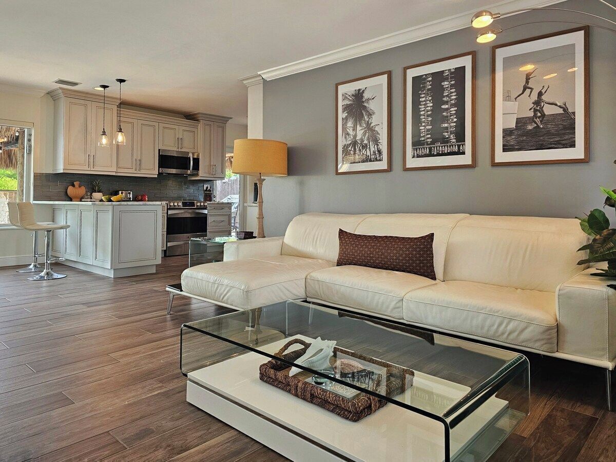 Una sala de estar moderna con una mesa de centro de vidrio, un sofá blanco y una cocina al fondo.