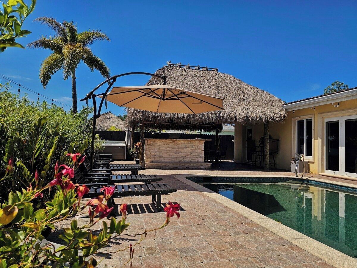 A poolside area with a thatched-roof structure, lounge chairs, and a swimming pool.