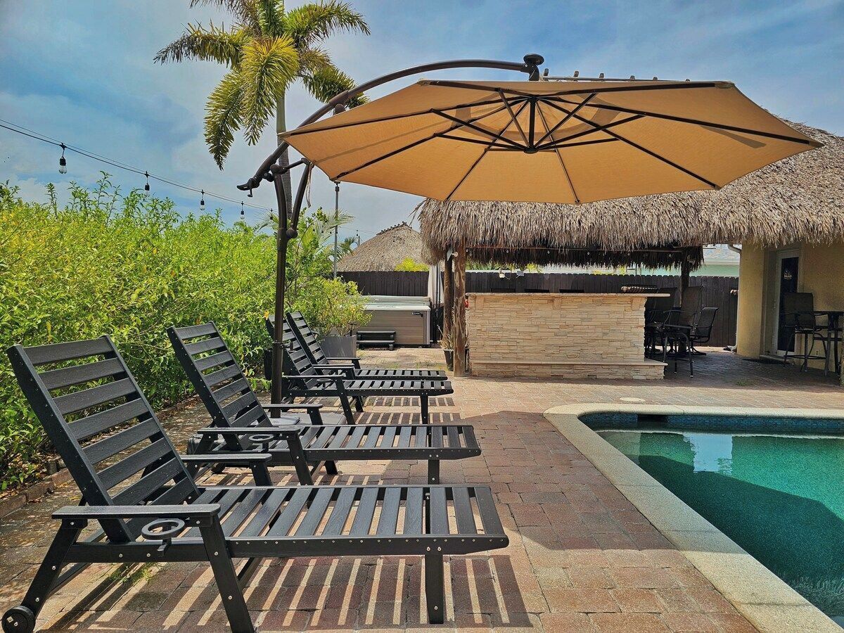 A poolside area with lounge chairs, a thatched-roof structure, and a pool.