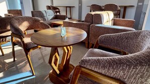 A modern lounge area with sofas and a round wooden table, large windows, and a flat-screen TV mounted on the wall. - Moonlight Hotel (Dar es Salaam)