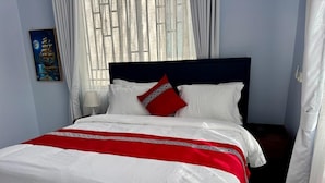 A bed with white bedding and a red accent, a nightstand with a lamp, and a painting on the wall. - Moonlight Hotel (Dar es Salaam)