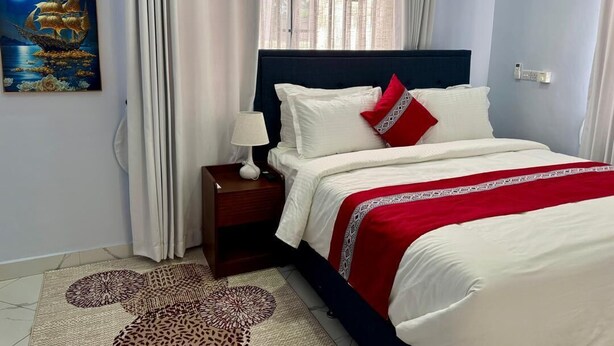 A bedroom with a bed, nightstand, lamp, and a painting on the wall. - Moonlight Hotel (Dar es Salaam)