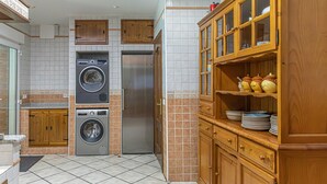 Eine Küche mit Waschmaschine, Kühlschrank, Holzschränken und Fliesenboden.