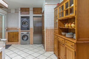 A kitchen with a washing machine, a refrigerator, wooden cabinets, and a tiled floor.